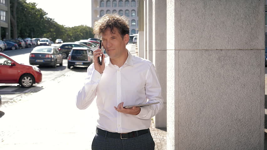 Handsome man with white shirt talking on the phone walking with tablet