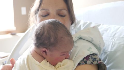 A tired young mother burps her newborn girl after nursing her in the hospital