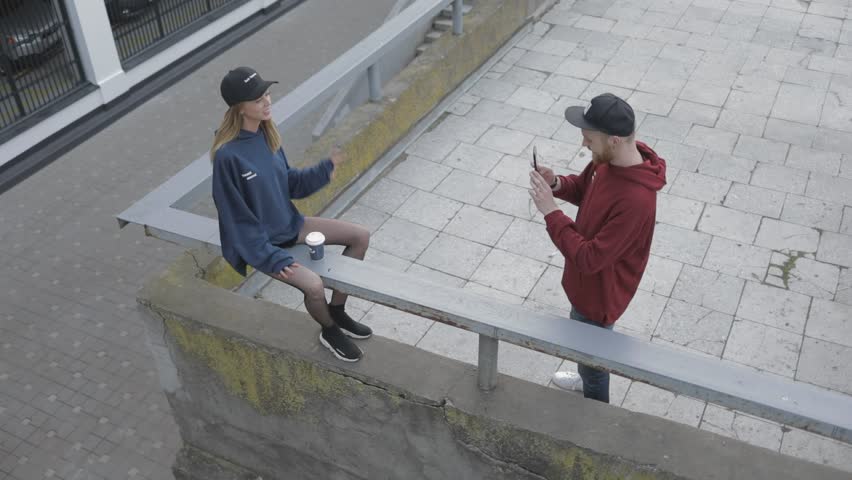 Young man taking pictures of his girlfriend whirling on camera. Beautiful couple having fun outdoors by making photos on smartphone in the european city center.