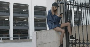 Beautiful young woman reads and writes messages on a smartphone. A handsome guy walks past a girl in a sweatshirt. City urban style. 4K video shooting by handheld gimbal