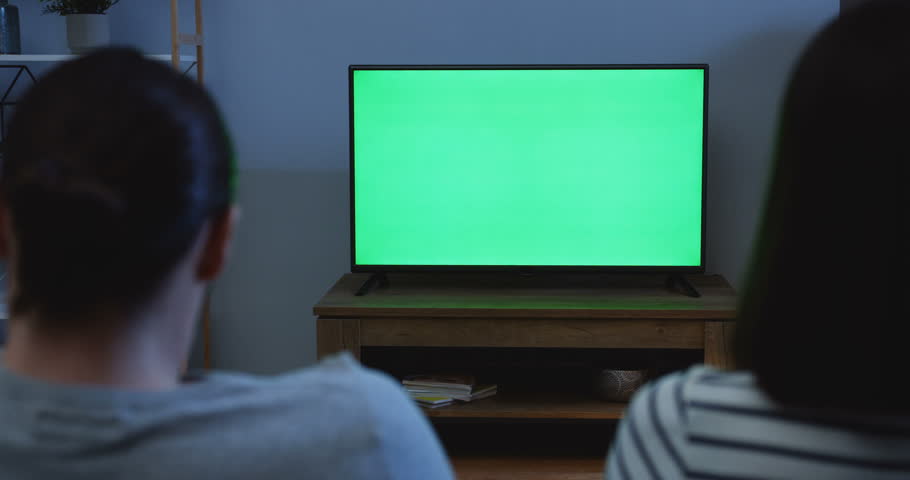 Rear of the couple watching TV with green screen and changing channels late at night in the living room. Indoors