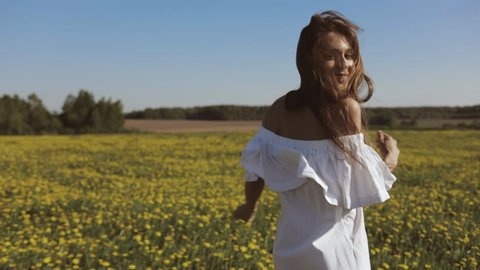 Attractive Young Woman Walks through the meadow and looks at Camera. Outdoor lifestyle portrait. Slow motion video shooting by handheld gimbal