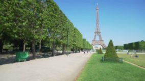 Wide shot of the Eiffel Tower in front of the Champs de Mars park in Paris. Blurred view of the Field of Mars and the historic Eiffel Tower in France