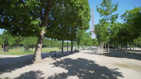 The Field of Mars park in front of the Eiffel Tower in Paris. Scenic view of famous French monument behind large field of trees