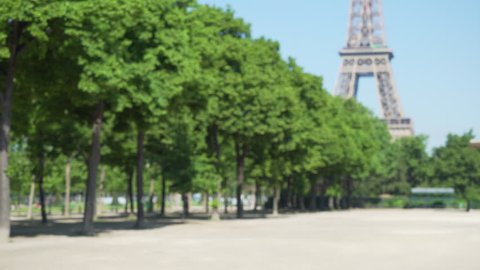 Defocused background plate of trees on the Champs de Mars with the Eiffel Tower behind. View of flat open park with historic French landmark in the distance