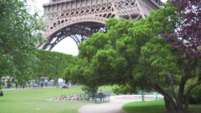 View of the Eiffel Tower covered by luscious green trees at Champs de Mars. Large open park Field of Mars next to historic French landmark in Paris