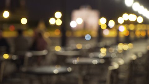 Bokeh lights on out of focus outdoor cafe. Blurry exterior night scene at restaurant with tables and chairs