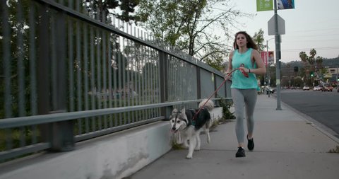 Millennial Female in Teal Running with Husky Dog with Smart Watch