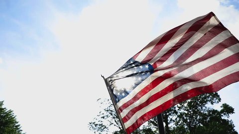 American flag in neighborhood flies in wind from low angle slow motion right justified