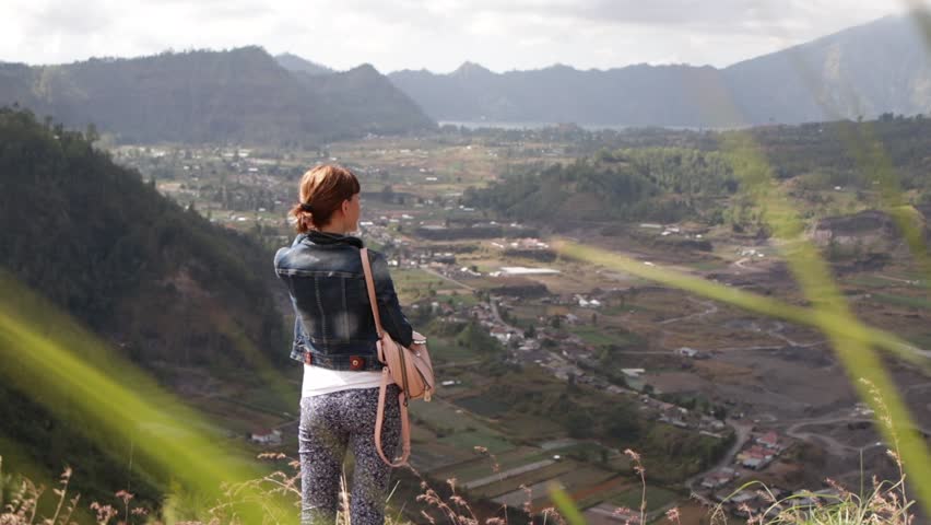 Young woman with smartphone and backpack on a beautiful mountain background. Volcano Batur, Bali.