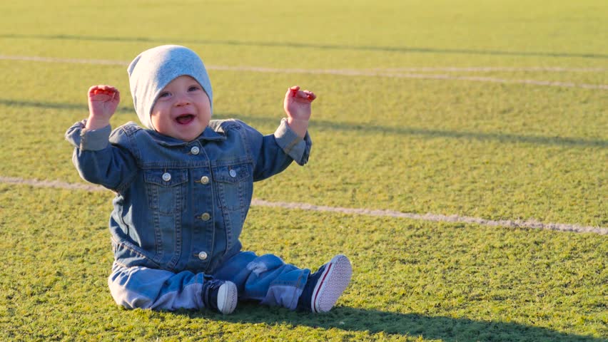 Cute baby boy sitting at football field. Active childhood concept.
