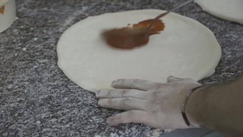 Pouring tomato sauce on pizza dough 
