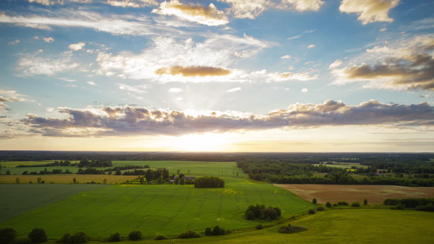 Drone lapse beautiful countryside scenery, cultivated green fields and colorful sunset horizon with yellow blue sky fast moving clouds, time lapse up motion  Royalty-Free Stock Footage #1011800339