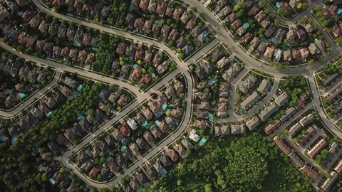 Aerial drone flight over a suburban community on a sunny summer day.  Roofs and backyard pools look bright and colorful. Trees and lawns are lush and green.
