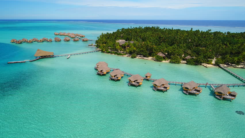 Aerial view of Motu Tautau, palm trees on little islets and turquoise water of blue lagoon, over water bungalows, tropical paradise of South Pacific Ocean - Tahaa island, landscape of French Polynesia