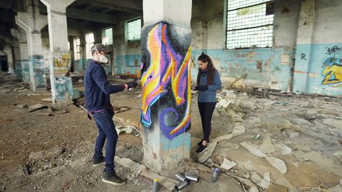 Time-lapse of graffiti artists are using aerosol paint to decorate abandoned industrial building with modern graffiti images. Creativity, street art and people concept.