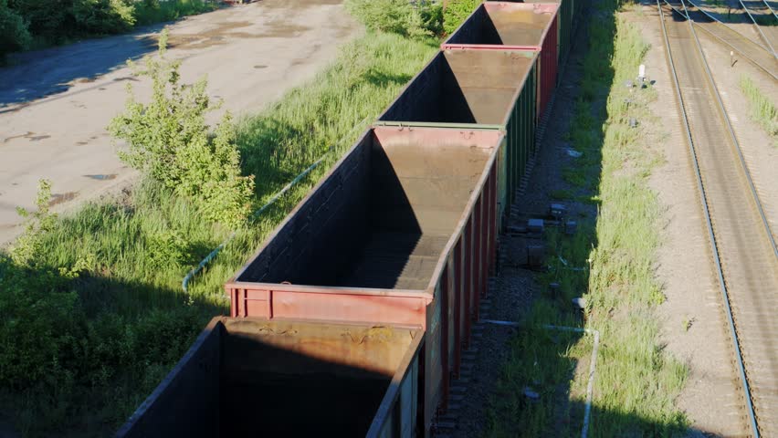 Empty cargo freight train wagoons go on railroad in industrial zone, view from above