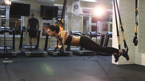 Young attractive woman does core abs oblique training with fitness straps in the gym's studio, trx.