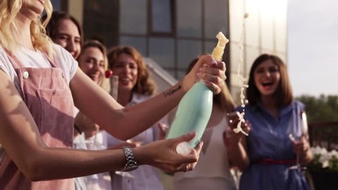 Beautiful young ladies celebrate. Hen-party. Shaking a bizarre bottle of champagne and letting it spraying. The girl pours a drink into glasses. Outside. Glamorous party. Slow motion