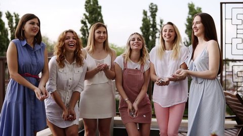 Stylish girls on bachelorette party outside on the terrace. Throw silver confetti into the air. Happy lifestyle, enjoy life. Dancing and laughing. Daytime. Slow motion