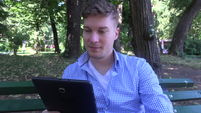 Boy happy young male sitting on bench in nature looking on tablet leisure time 