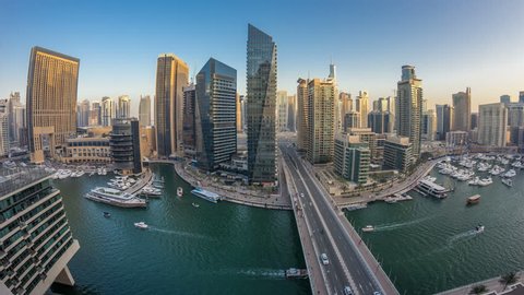 Beautiful aerial top view day to night transition timelapse of all Dubai Marina promenade and canal with floating yachts and boats after sunset in Dubai, UAE. Modern towers and traffic on the bridge.
