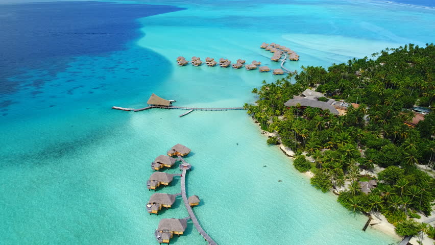 Aerial view of Motu Tautau, palm trees on little islets and turquoise water of blue lagoon, over water bungalows, tropical paradise of South Pacific Ocean - Tahaa island, seascape of French Polynesia