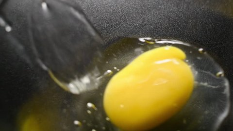 Smoothly sliding yellow egg yolk in black cooking pan . Shot is in high speed. 