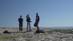 Three young men stand on top of a mountain and look at the landscape