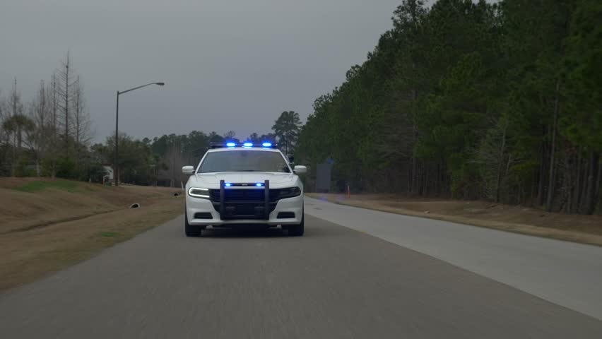 A police squad car drives with its blue lights flashing to pull over another car. | Shutterstock HD Video #1011846995