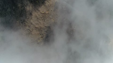Aerial top down view of volcanic landscape first showing thick clouds then showing cooled down lava flows and in between the fertile soil with vegetation on landscape also showing road to Mount Etna