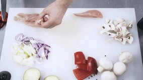Top view of an unrecognizable chefs hands slicing a chicken on a cutting board for pizza production. Locked down real time medium shot