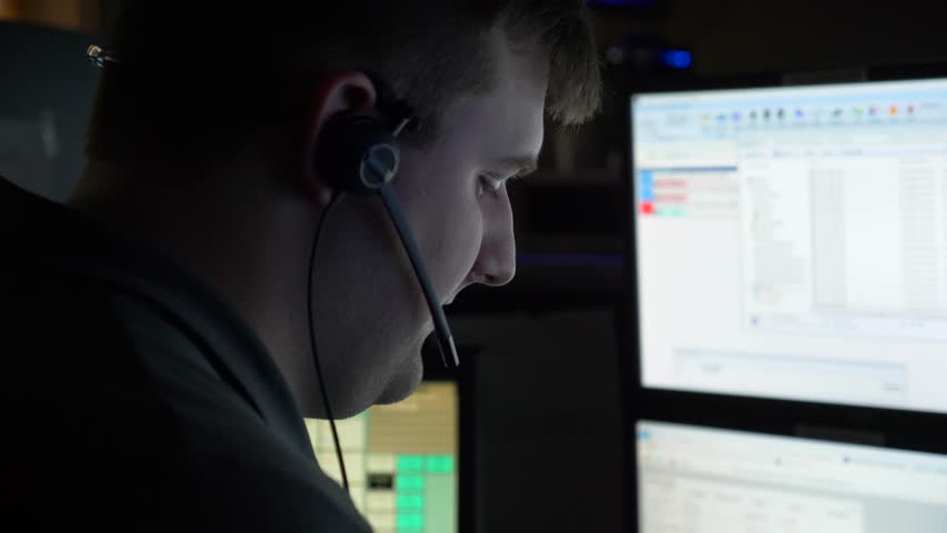 A 911 dispatcher works at his computer station at a control center to help respond to emergency calls. Royalty-Free Stock Footage #1011852584