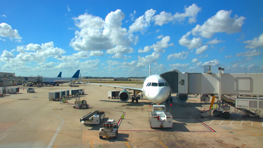 Generic Airport Concourse Exterior with Parked Airliners with Ground Support Vehicles Driving Around on a Sunny Day with White Clouds in a Blue Sky Royalty-Free Stock Footage #1011853658
