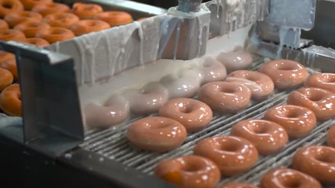 This video shows a fresh batch of donuts being glazed by machine in donut factory assembly line.