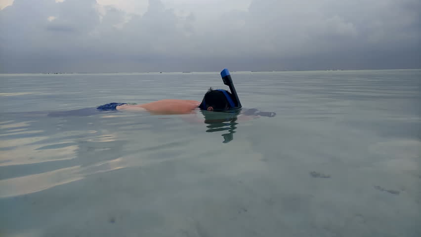 A man swims under the water with a mask for diving and shoots video on camera, shooting fish, sharks.