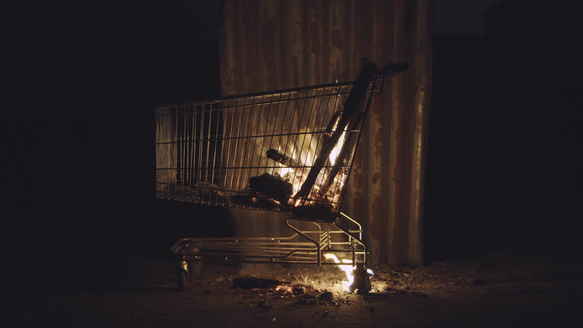 Wood Burning Inside A Shopping Cart In A Desolated City Homeless Area With A Corrugated Iron Sheet Leaning Against It As  Windbreaker. Royalty-Free Stock Footage #1011880088