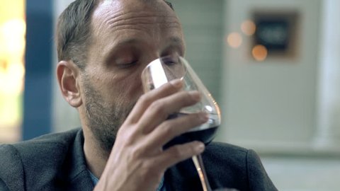 Sad, drunk man drinking red wine sitting in cafe