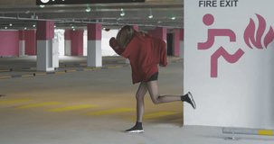 Long-haired young woman in a red hoodie sweatshirt having fun, turning to camera, and smiling in a bright sunshine. City urban style. 4K video shooting by handheld gimbal
