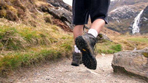 4K Young traveller walking through the Scottish Highlands. Close up of Mans legs and boots path hiking and back pack nature trekking through mountains toward a waterfall.Scotland UK Glencoe 