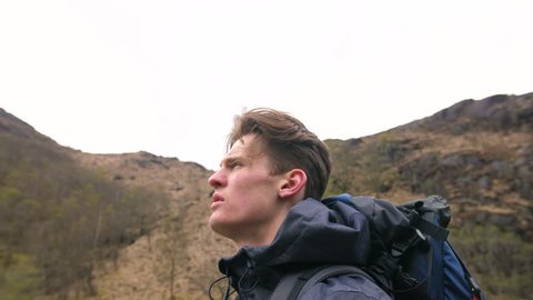 4K close up side profile of handsome traveller looking into the distance in Scottish Highlands.Trekker man  hiking through Scotland UK. 