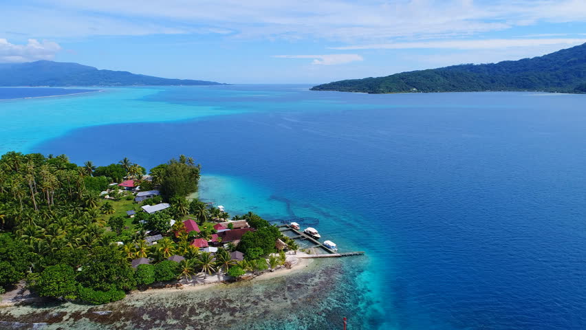 Aerial view of coral barrier reef around Tahaa island, palm trees on little islet Motu Atger and turquoise clear water of blue lagoon - South Pacific Ocean, seascape of French Polynesia from above