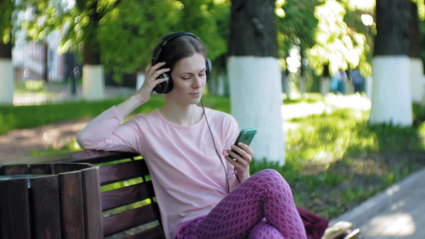 young stylish beautiful woman, on city streets listening to music in large monitor headphones. 4k