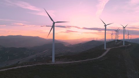 Wind turbine eco farm on beautiful purple evening mountain landscape. Renewable energy production for green ecological world. Aerial view of wind mills farm park on evening mountain. Lateral flight