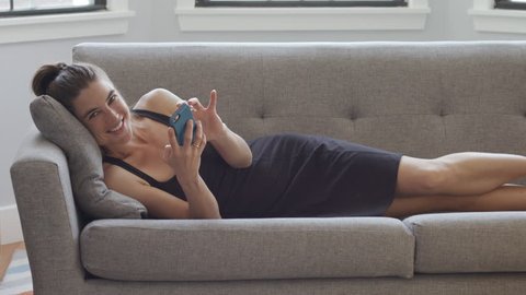 A pretty young woman using her smartphone on the couch, texting while relaxing, 4K slow motion