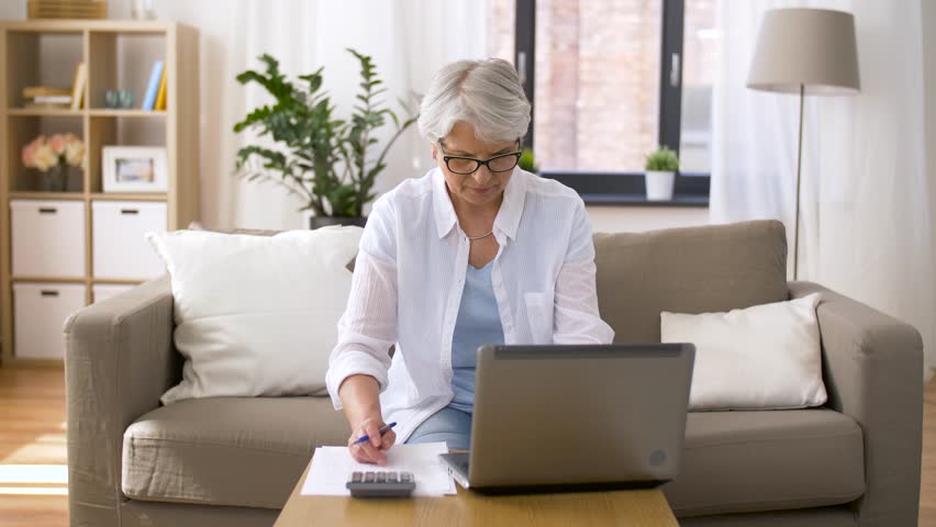 Business, accountancy and people concept - senior woman with papers or bills, laptop computer and calculator at home | Shutterstock HD Video #1011900902