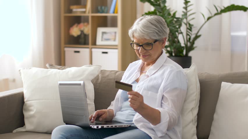 Technology, online shopping and people concept - happy senior woman in glasses with laptop computer and credit or bank card at home | Shutterstock HD Video #1011901013