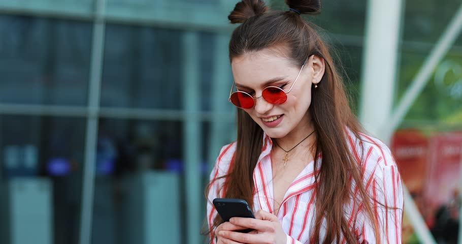 Young woman typing message on the phone standing near a shopping center. Woman in pink sunglasses sunny day blogging internet surfing virtual world mobile device summer vacation Royalty-Free Stock Footage #1011905522