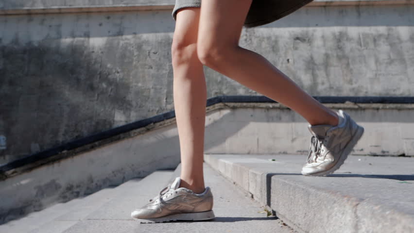Close up of woman's legs in sneakers. GIrl goes down the city stairs. Slow motion.