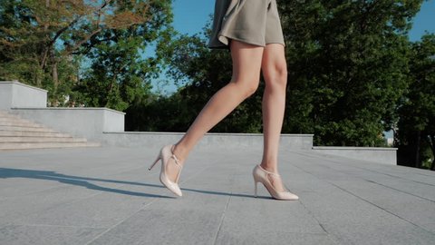 Sexy legs with high beige heels goes down the stairs of big city. Roamntic woman walking on boulvard alone. Attractive girl in short dress at summer season. Slow motion.